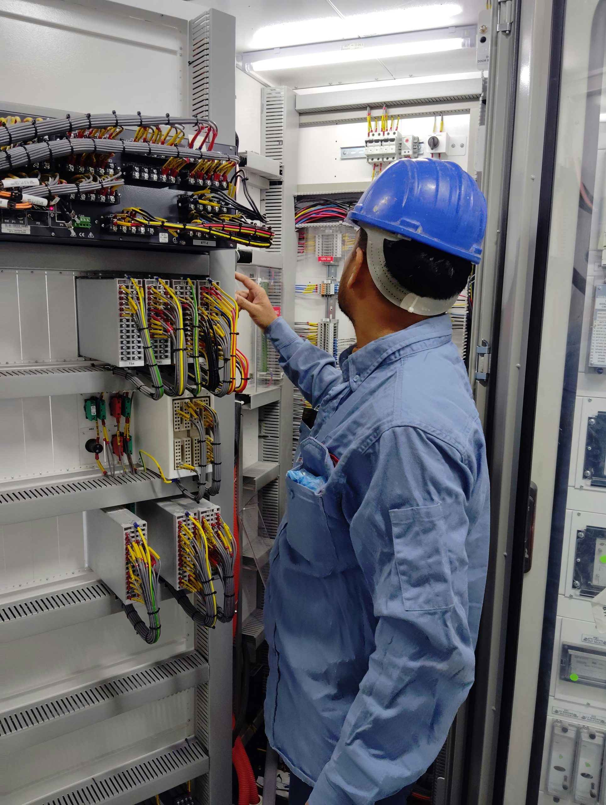 Acasa An electrician in a hard hat inspecting a control panel inside an industrial setting, ensuring safety and functionality.